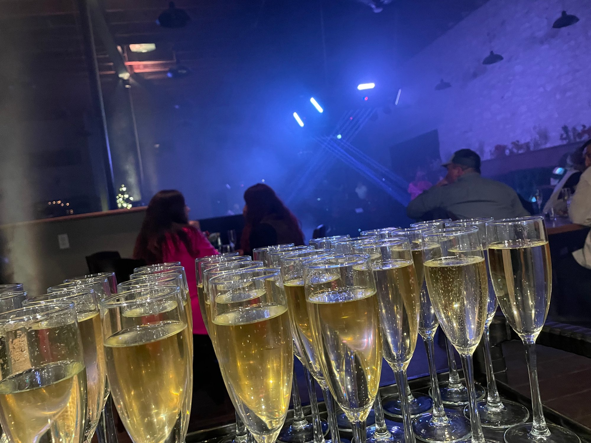 Champagne flutes filled with sparkling wine lined up on a tray with blue stage lights in the background.